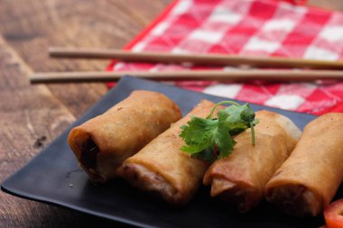 Tayland 'da kahverengi ahşap bir masada doğranmış domatesli siyah kare bir tabakta kızarmış börek servis ediliyor..