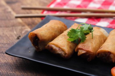 Tayland 'da kahverengi ahşap bir masada doğranmış domatesli siyah kare bir tabakta kızarmış börek servis ediliyor..