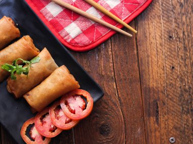 Tayland 'da kahverengi ahşap bir masada doğranmış domatesli siyah kare bir tabakta kızarmış börek servis ediliyor..