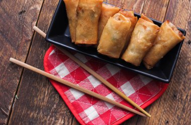 Tayland 'da kahverengi ahşap bir masada doğranmış domatesli siyah kare bir tabakta kızarmış börek servis ediliyor..