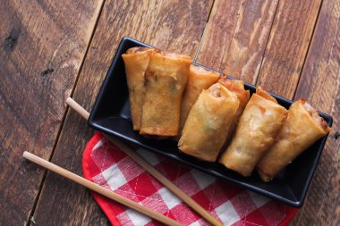 Tayland 'da kahverengi ahşap bir masada doğranmış domatesli siyah kare bir tabakta kızarmış börek servis ediliyor..