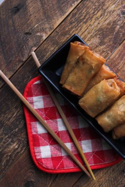 Tayland 'da kahverengi ahşap bir masada doğranmış domatesli siyah kare bir tabakta kızarmış börek servis ediliyor..