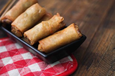 Tayland 'da kahverengi ahşap bir masada doğranmış domatesli siyah kare bir tabakta kızarmış börek servis ediliyor..