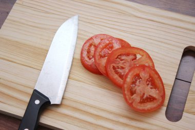 Dilimlenmiş domates ve bıçaklar ahşap bir masadaki tahta kesme tahtasına konur..