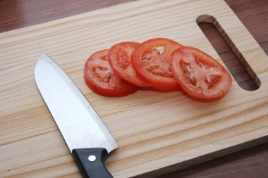 Dilimlenmiş domates ve bıçaklar ahşap bir masadaki tahta kesme tahtasına konur..