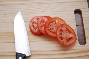 Dilimlenmiş domates ve bıçaklar ahşap bir masadaki tahta kesme tahtasına konur..