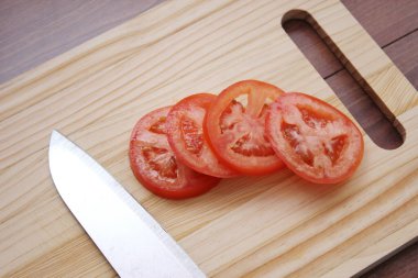 Dilimlenmiş domates ve bıçaklar ahşap bir masadaki tahta kesme tahtasına konur..