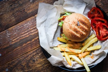 Tahta masada patates kızartması ve domatesle servis edilen ev yapımı hamburgerler. Fast food ve abur cubur.