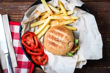 Tahta masada patates kızartması ve domatesle servis edilen ev yapımı hamburgerler. Fast food ve abur cubur.