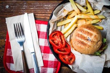 Tahta masada patates kızartması ve domatesle servis edilen ev yapımı hamburgerler. Fast food ve abur cubur.