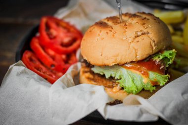 Tahta masada patates kızartması ve domatesle servis edilen ev yapımı hamburgerler. Fast food ve abur cubur.