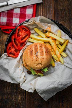 Tahta masada patates kızartması ve domatesle servis edilen ev yapımı hamburgerler. Fast food ve abur cubur.