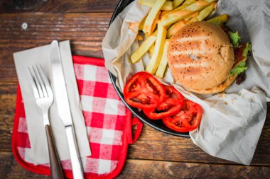 Tahta masada patates kızartması ve domatesle servis edilen ev yapımı hamburgerler. Fast food ve abur cubur.
