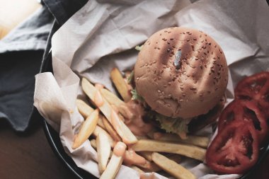 Tahta masada patates kızartması ve domatesle servis edilen ev yapımı hamburgerler. Fast food ve abur cubur. Modern tonda.