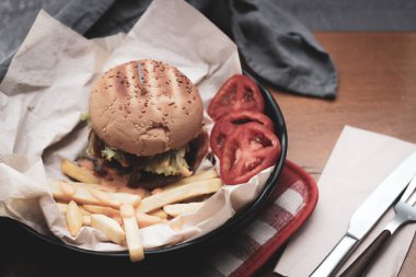 Tahta masada patates kızartması ve domatesle servis edilen ev yapımı hamburgerler. Fast food ve abur cubur. Modern tonda.