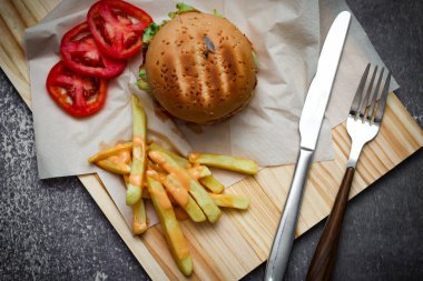 Tahta masada patates kızartması ve domatesle servis edilen ev yapımı hamburgerler. Fast food ve abur cubur.