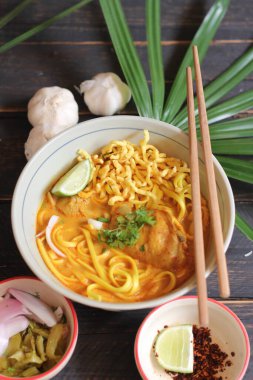 Khao Soi Recipe, Khao Soi, Khao Soi Kai, Thai Erişte Khao Soi, Baharatlı Tavuk Köri Dekoratif yapraklı siyah ahşap masa, dikey fotoğraf.