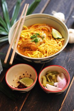 Khao Soi Recipe, Khao Soi, Khao Soi Kai, Thai Erişte Khao Soi, Baharatlı Tavuk Köri Dekoratif yapraklı siyah ahşap masa, dikey fotoğraf.