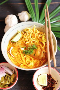 Khao Soi Recipe, Khao Soi, Khao Soi Kai, Thai Erişte Khao Soi, Baharatlı Tavuk Köri Dekoratif yapraklı siyah ahşap masa, dikey fotoğraf.