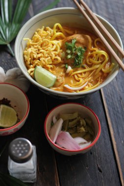 Khao Soi Recipe, Khao Soi, Khao Soi Kai, Thai Erişte Khao Soi, Baharatlı Tavuk Köri Dekoratif yapraklı siyah ahşap masa, dikey fotoğraf.