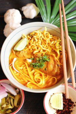 Khao Soi Recipe, Khao Soi, Khao Soi Kai, Thai Erişte Khao Soi, Baharatlı Tavuk Köri Dekoratif yapraklı siyah ahşap masa, dikey fotoğraf.