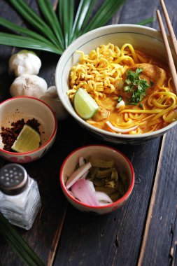 Khao Soi Recipe, Khao Soi, Khao Soi Kai, Thai Erişte Khao Soi, Baharatlı Tavuk Köri Dekoratif yapraklı siyah ahşap masa, dikey fotoğraf.