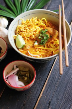Khao Soi Recipe, Khao Soi, Khao Soi Kai, Thai Erişte Khao Soi, Baharatlı Tavuk Köri Dekoratif yapraklı siyah ahşap masa, dikey fotoğraf.