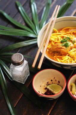 Khao Soi Recipe, Khao Soi, Khao Soi Kai, Thai Erişte Khao Soi, Baharatlı Tavuk Köri Dekoratif yapraklı siyah ahşap masa, dikey fotoğraf.
