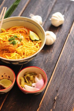 Khao Soi Recipe, Khao Soi, Khao Soi Kai, Thai Erişte Khao Soi, Baharatlı Tavuk Köri Dekoratif yapraklı siyah ahşap masa, dikey fotoğraf.
