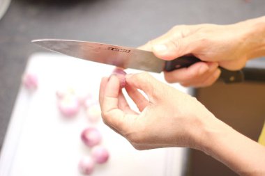 Bir kadının eli, beyaz plastik bir kesme tahtasındaki soğanları kesiyor..