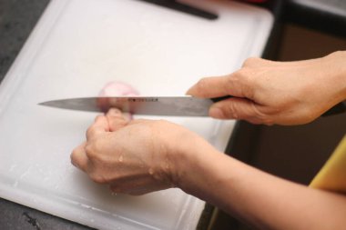 Bir kadının eli, beyaz plastik bir kesme tahtasındaki soğanları kesiyor..
