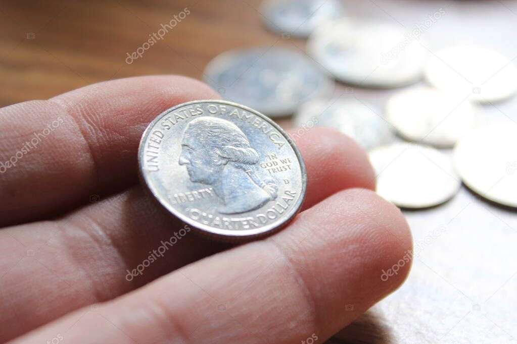 hand picking up a quarter coin in american currency spread on the wooden floor