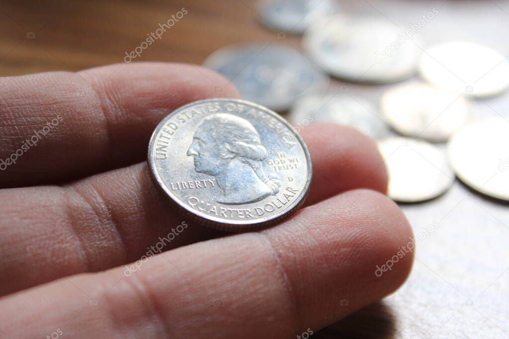 hand picking up a quarter coin in american currency spread on the wooden floor