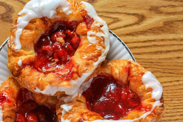 Cherry filled Danish or Danish bread served in a white plate on a brown wooden table.