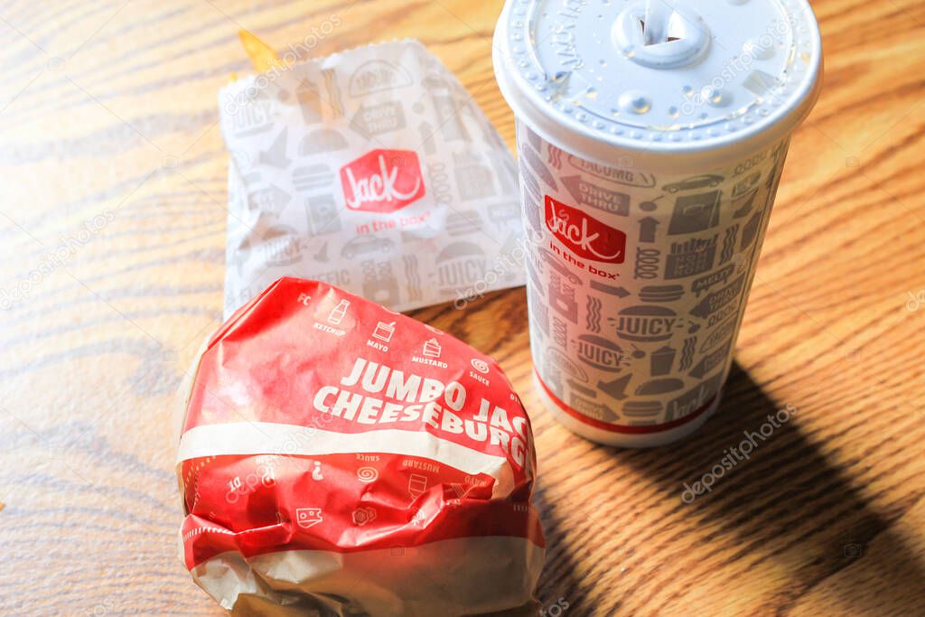 WASHINGTON, USA - MARCH, 15 2022 : Jack in the box hamburgers, french fries and glasses served on a brown wooden table.