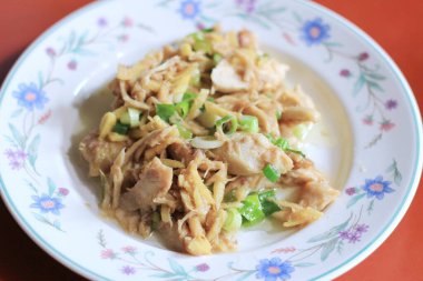 Turuncu bir yemek masasında beyaz bir çiçek tabağında servis edilen doğranmış taze soğanlı zencefilli kızarmış tavuk..