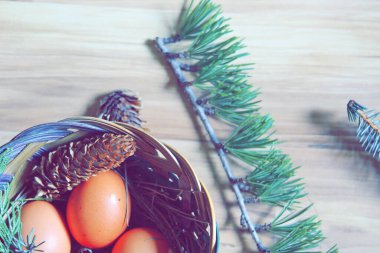 Çam yaprakları, kozalaklar ve açık kahverengi ahşap zemine yerleştirilmiş dallarla dolu bir sepette yumurtalar..