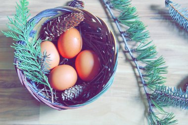 Çam yaprakları, kozalaklar ve açık kahverengi ahşap zemine yerleştirilmiş dallarla dolu bir sepette yumurtalar..