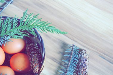 Çam yaprakları, kozalaklar ve açık kahverengi ahşap zemine yerleştirilmiş dallarla dolu bir sepette yumurtalar..