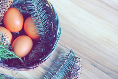 Çam dalları ve modern tonlarda çam kozalakları olan bir sepette paskalya yumurtaları..