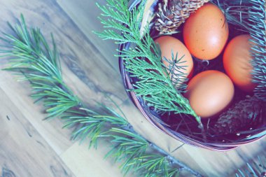 Çam dalları ve modern tonlarda çam kozalakları olan bir sepette paskalya yumurtaları..