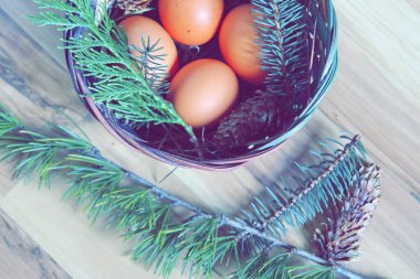 Çam dalları ve modern tonlarda çam kozalakları olan bir sepette paskalya yumurtaları..