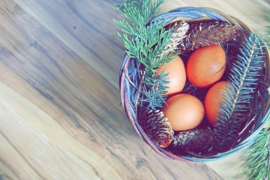 Çam dalları ve modern tonlarda çam kozalakları olan bir sepette paskalya yumurtaları..