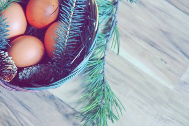 Çam dalları ve modern tonlarda çam kozalakları olan bir sepette paskalya yumurtaları..