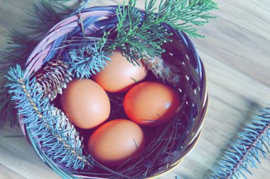 Çam dalları ve modern tonlarda çam kozalakları olan bir sepette paskalya yumurtaları..