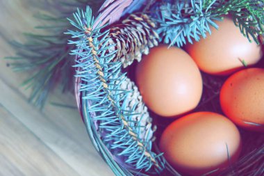 Çam dalları ve modern tonlarda çam kozalakları olan bir sepette paskalya yumurtaları..