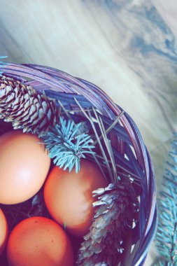 Çam dalları ve modern tonlarda çam kozalakları olan bir sepette paskalya yumurtaları..