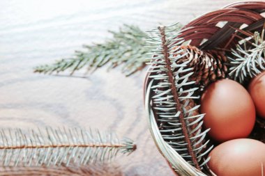 Paskalya yumurtaları sepetin içinde, çam dalları ve kozalaklar ahşap zemine yerleştirilmiş, modern ton..