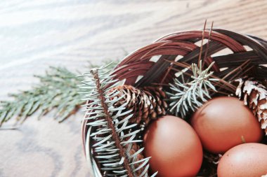 Paskalya yumurtaları sepetin içinde, çam dalları ve kozalaklar ahşap zemine yerleştirilmiş, modern ton..