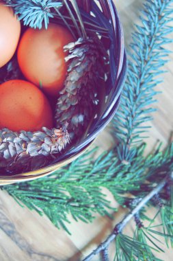 Çam dalları ve modern tonlarda çam kozalakları olan bir sepette paskalya yumurtaları..